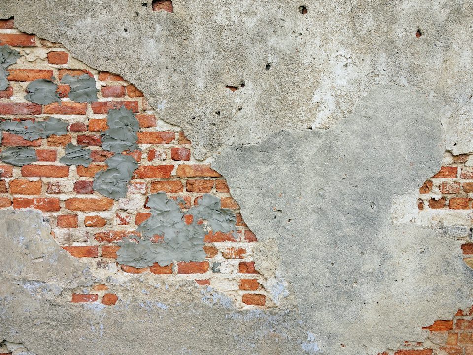 A weathered wall where the grey coating has broken away
